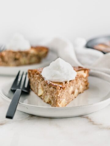 slice of healthy apple cake topped with whipped cream on a grey plate with a black fork.