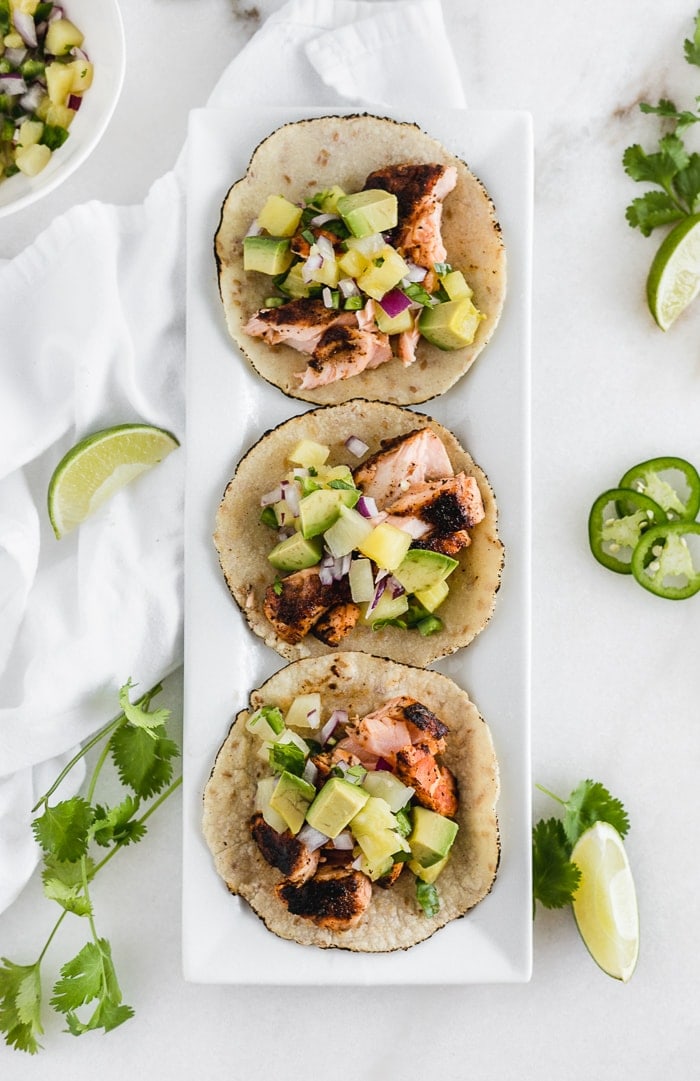 Three blackened salmon tacos with pineapple salsa on a plate.