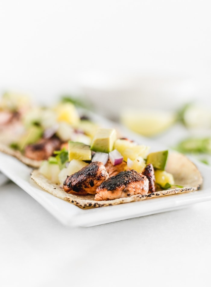 Close up of three blackened salmon tacos with pineapple salsa on a plate.