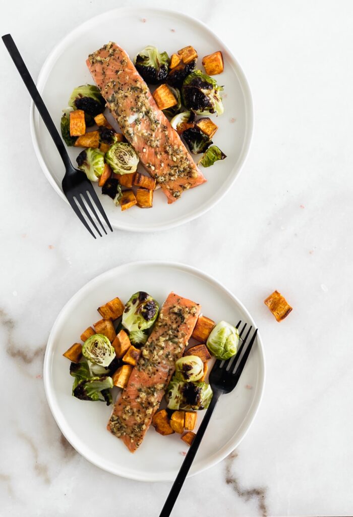 overhead view of 2 white plates with salmon, brussels sprouts and sweet potatoes on them with black forks.