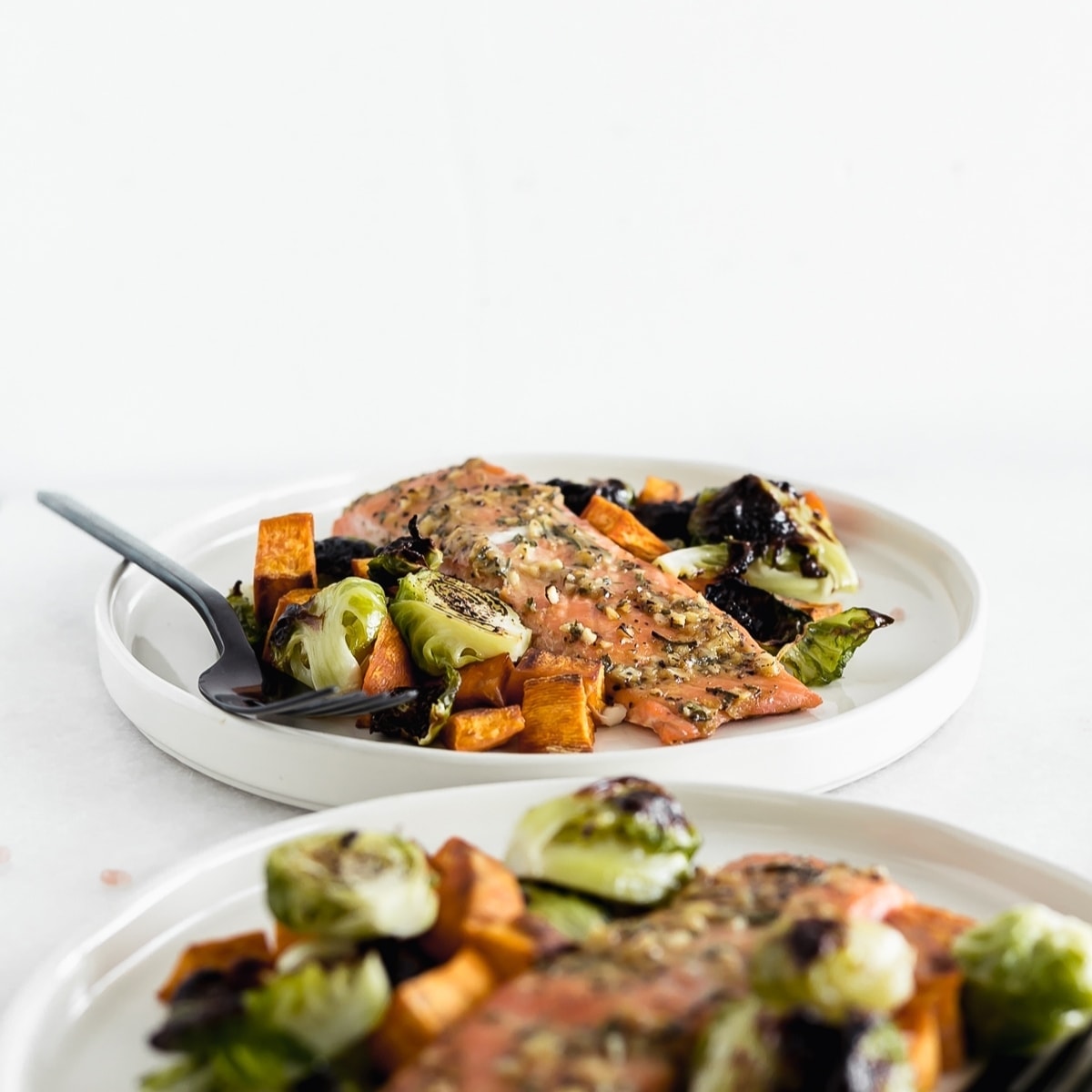 Filet of maple dijon salmon with brussels sprouts and sweet potatoes on a white plate with a black fork.