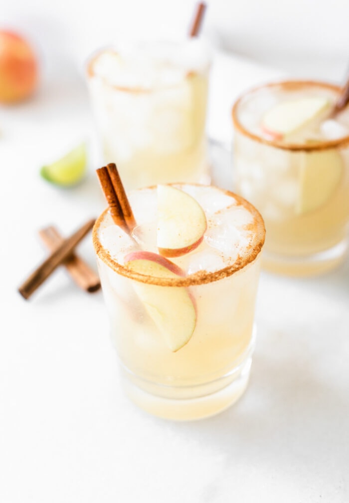 three Apple Cider Margaritas in cinnamon rimmed glasses with apple slices and cinnamon sticks in each.