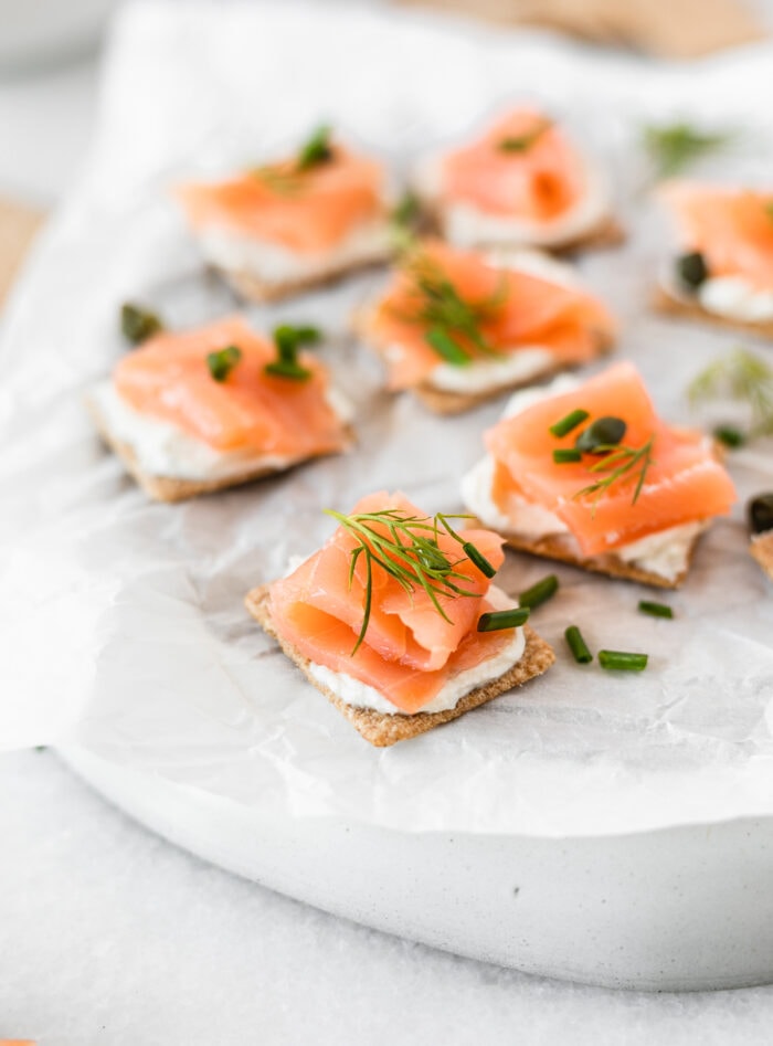 closeup of smoked salmon bites topped with fresh herbs on a white parchment covered plate.