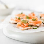 Smoked salmon bites topped with fresh herbs on a white parchment covered plate.