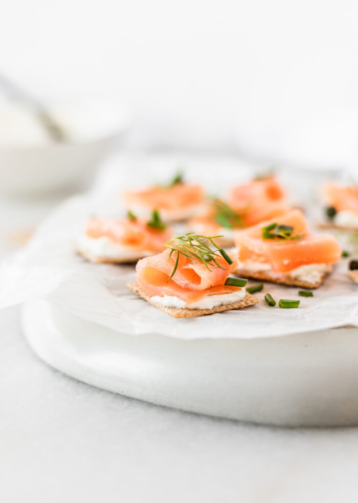 smoked salmon bites topped with fresh herbs on a white parchment covered plate.