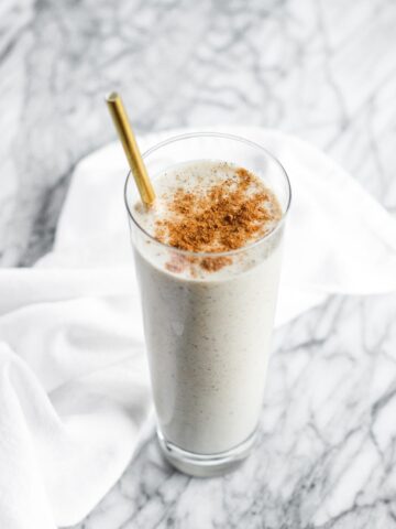 healthy gut vanilla chai smoothie in a clear glass topped with chai spice with a gold straw.