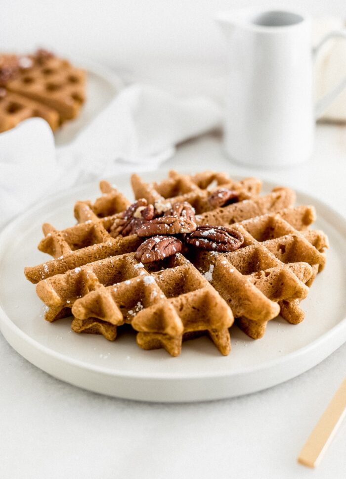 Healthy pumpkin waffle on a plate with pecans and powdered sugar on top.