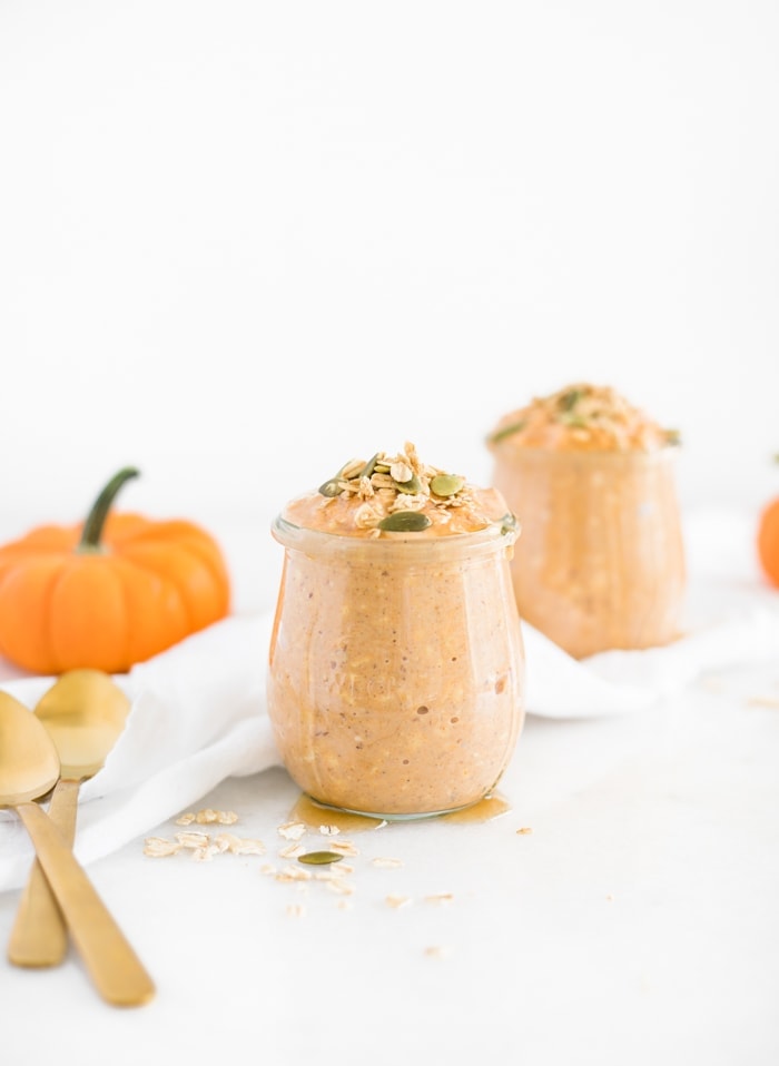 healthy pumpkin spice overnight oats in a jar topped with pumpkin seeds with another jar of oats and a pumpkin behind it.