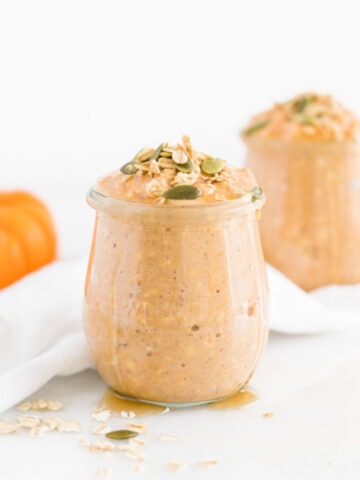 healthy pumpkin spice overnight oats in a jar with another jar and a small pumpkin in the background.