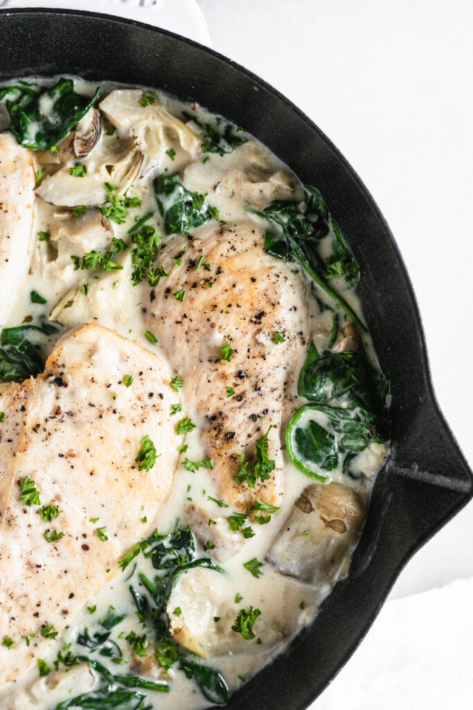 overhead closeup of spinach artichoke chicken in a cast iron skillet.