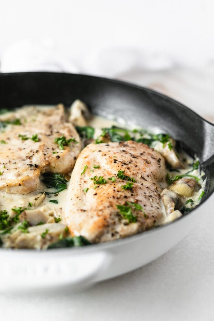 closeup of spinach artichoke chicken breast in a white cast iron skillet.