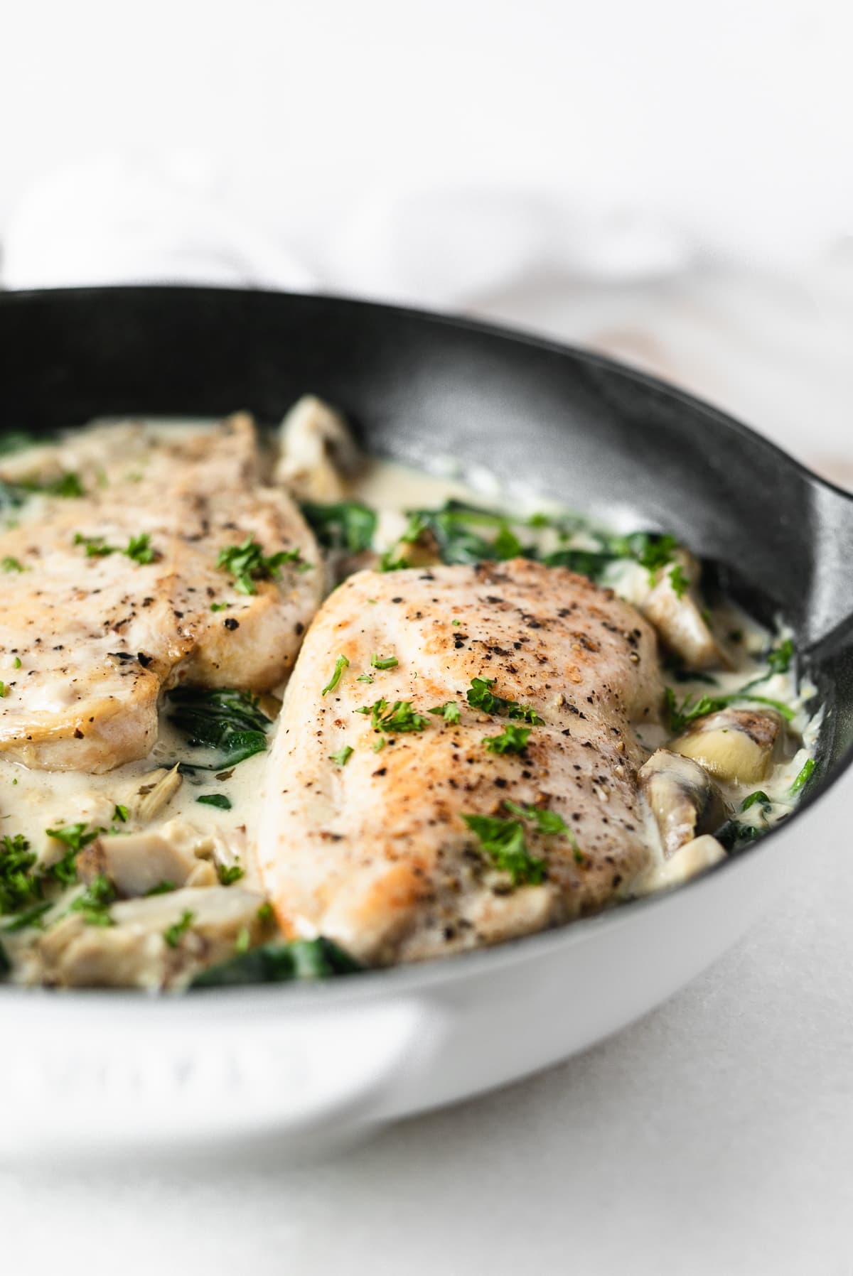 Closeup view of spinach artichoke chicken breast in a white cast iron skillet.