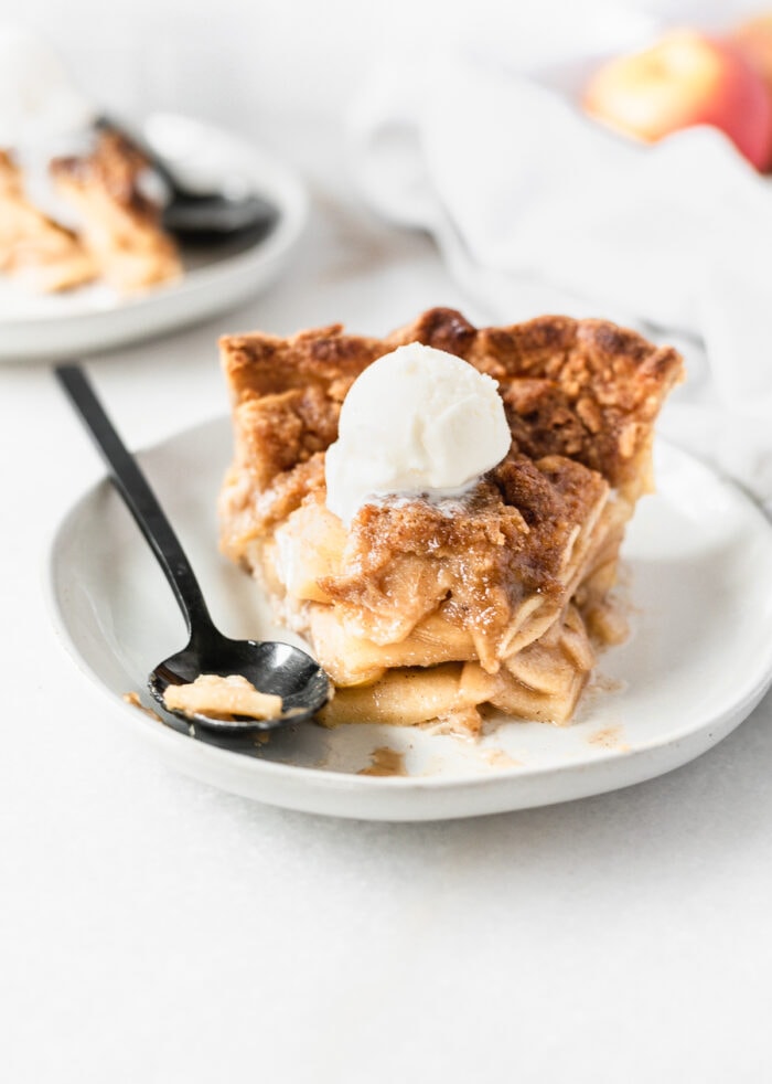 slice of apple crumb pie with a scoop of ice cream on top with a bite taken out and a black spoon next to it.