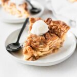 slice of apple crumb pie with a scoop of ice cream on top on a plate with a black spoon.