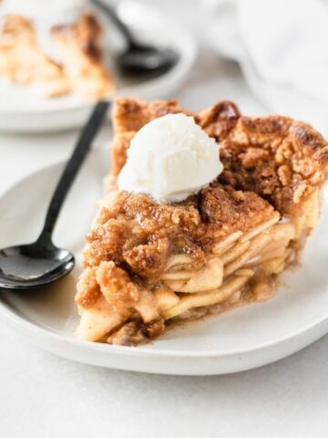 slice of apple crumb pie with a scoop of ice cream on top on a plate with a black spoon.
