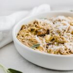 closeup of butternut squash sage chicken spaghetti covered with parmesan cheese in a white bowl.