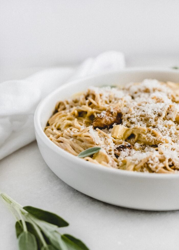 closeup of butternut squash sage chicken spaghetti covered with parmesan cheese in a white bowl.