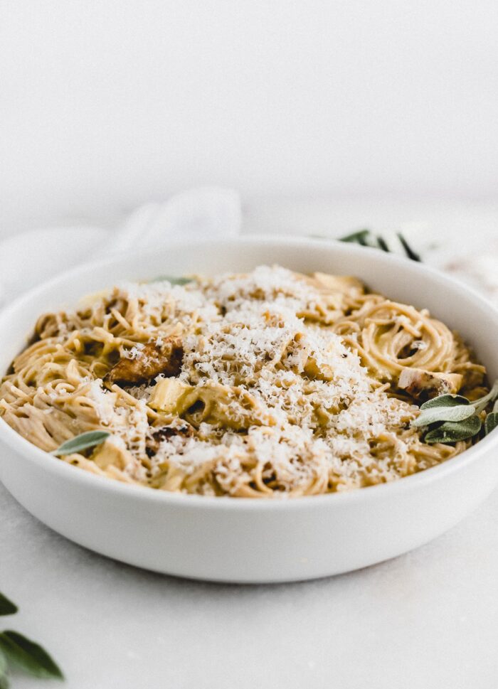butternut squash sage chicken spaghetti topped with parmesan cheese in a white bowl.