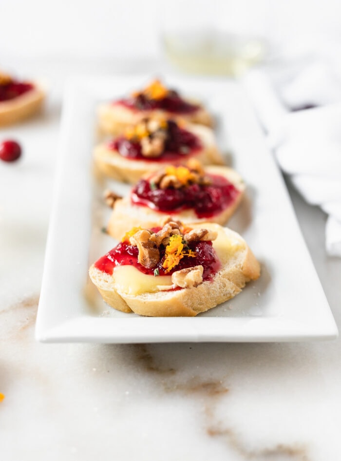 Cranberry Brie Crostini with walnuts and orange zest on a white serving dish.