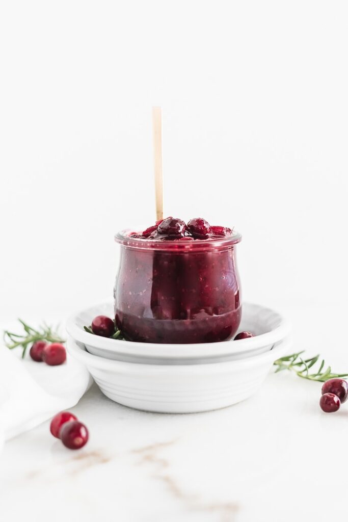 Lower sugar cranberry sauce in a clear glass container with a golden spoon inside of it with cranberry around it.