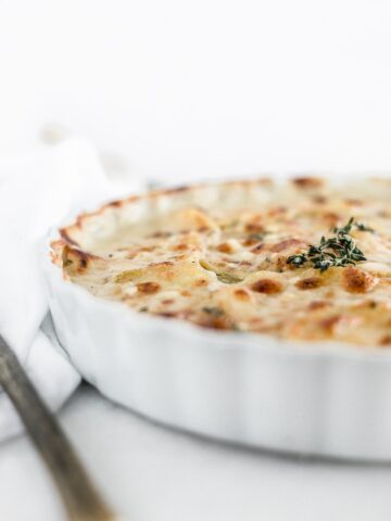 closeup of healthier cheesy scalloped potatoes in a white baking dish with thyme on top.