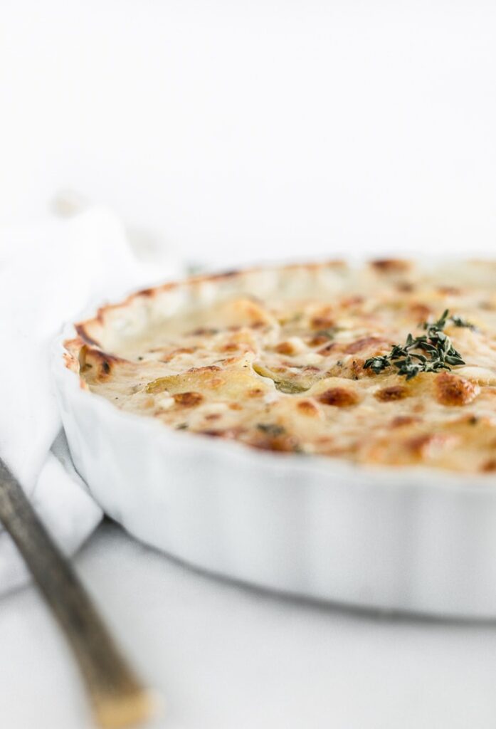 closeup of healthier cheesy scalloped potatoes in a white baking dish with thyme on top.