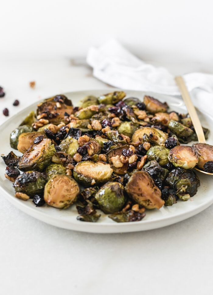 roasted brussels sprouts with cranberries and walnuts on a plate with a gold spoon.