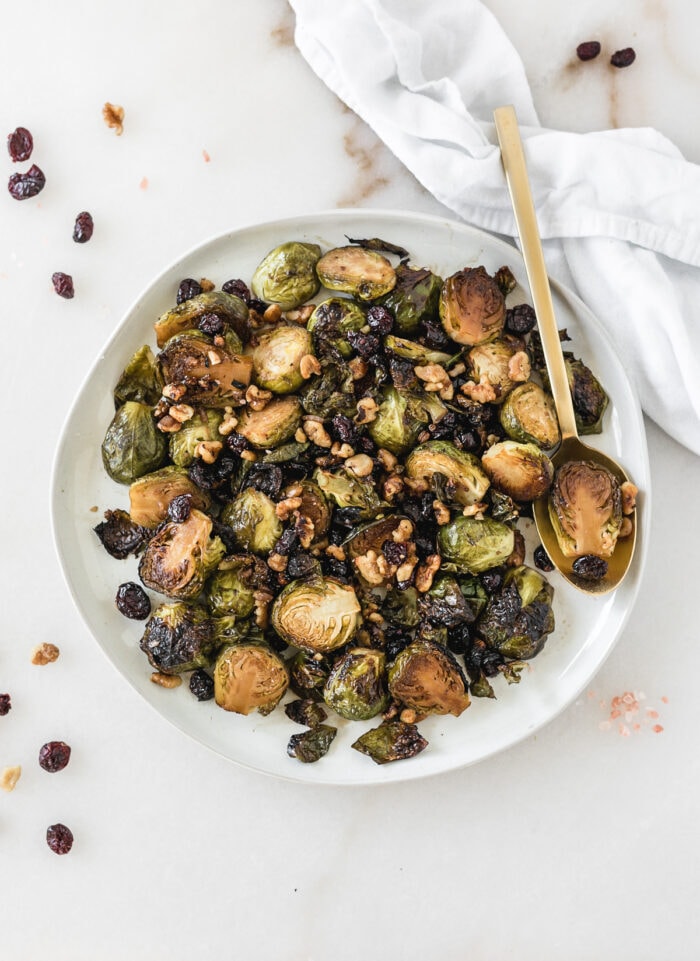 Christmas roasted brussels sprouts with cranberries and walnuts on a plate with a gold spoon.
