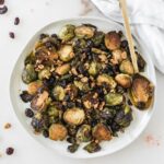 Christmas roasted brussels sprouts with cranberries and walnuts on a plate with a gold spoon.