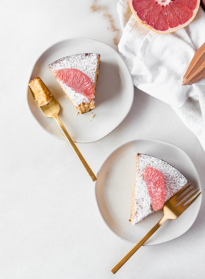 overhead view of two slices of grapefruit olive oil cake on plates with gold forks, with a bite taken from one slice.