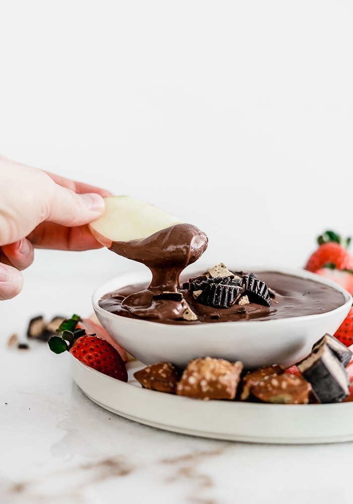 Hand dipping an apple slice into a bowl of Healthy Peanut Butter Cup Cheesecake Dip.