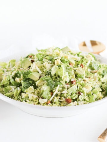 Chopped brussels sprout salad with parmesan, almonds, and avocado in a white bowl.