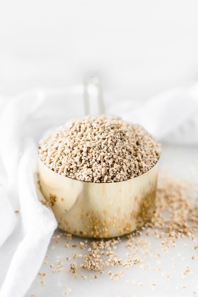 gold measuring cup filled with dry steel cut oats next to a white napkin.