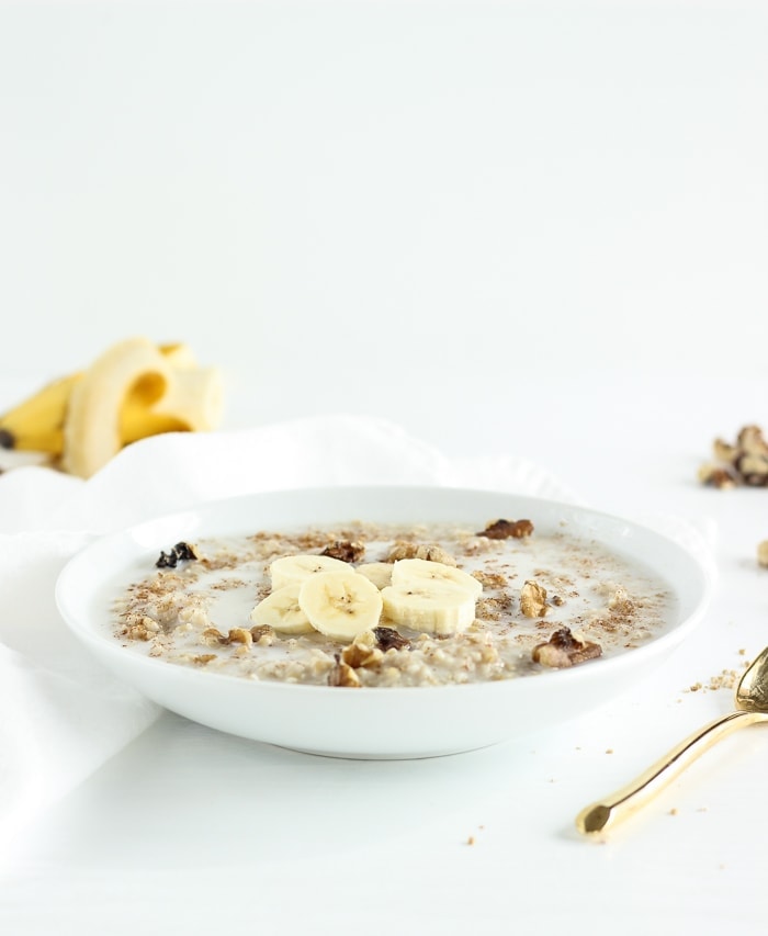 steel cut oatmeal in a white bowl topped with bananas, milk, and walnuts.