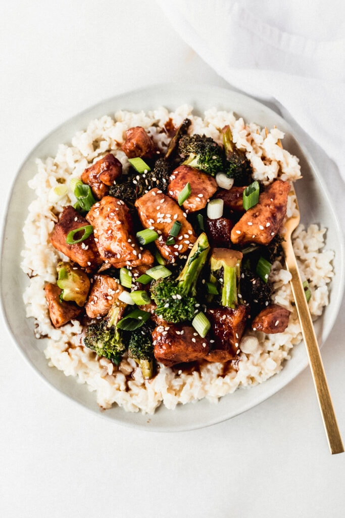 overhead view of sticky pomegranate ginger chicken with broccoli on top of coconut brown rice. 