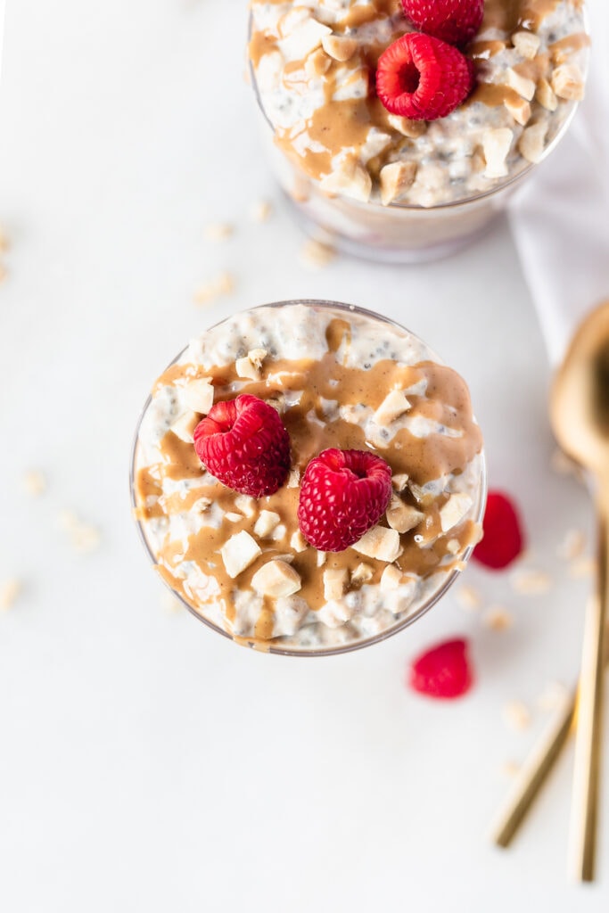 overhead view of pb&j overnight oats in a glass topped with fresh raspberries and peanut butter.