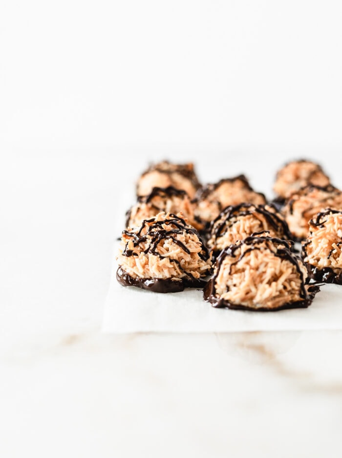 almond joy coconut macaroons drizzled with chocolate on a piece of parchment.