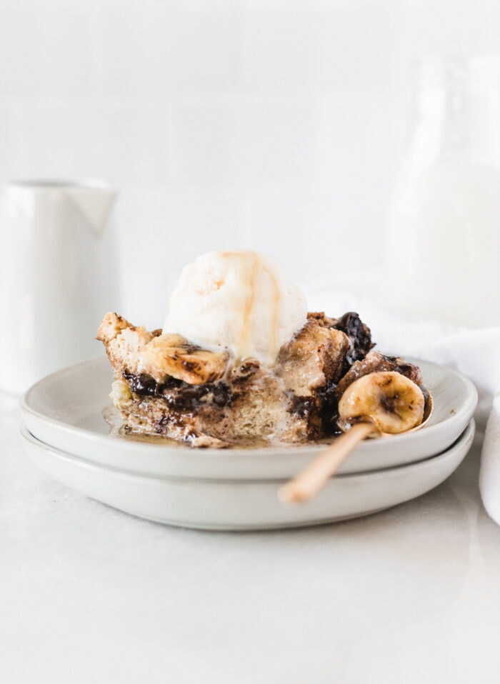 piece of banana bourbon chocolate chip bread pudding with bourbon sauce and a scoop of ice cream on two stacked plates with a bite scooped out into a spoon.