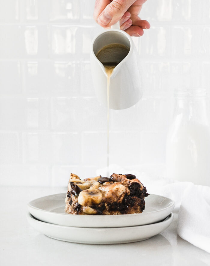 hand pouring whiskey sauce over a piece of bourbon banana chocolate chip bread pudding.