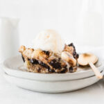 piece of banana bourbon chocolate chip bread pudding with bourbon sauce and a scoop of ice cream on two stacked plates.
