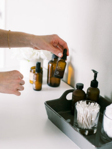 hand picking up an amber glass bottle of a serum from a vanity tray.