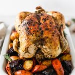 whole roasted chicken on top of root vegetables on a white platter.