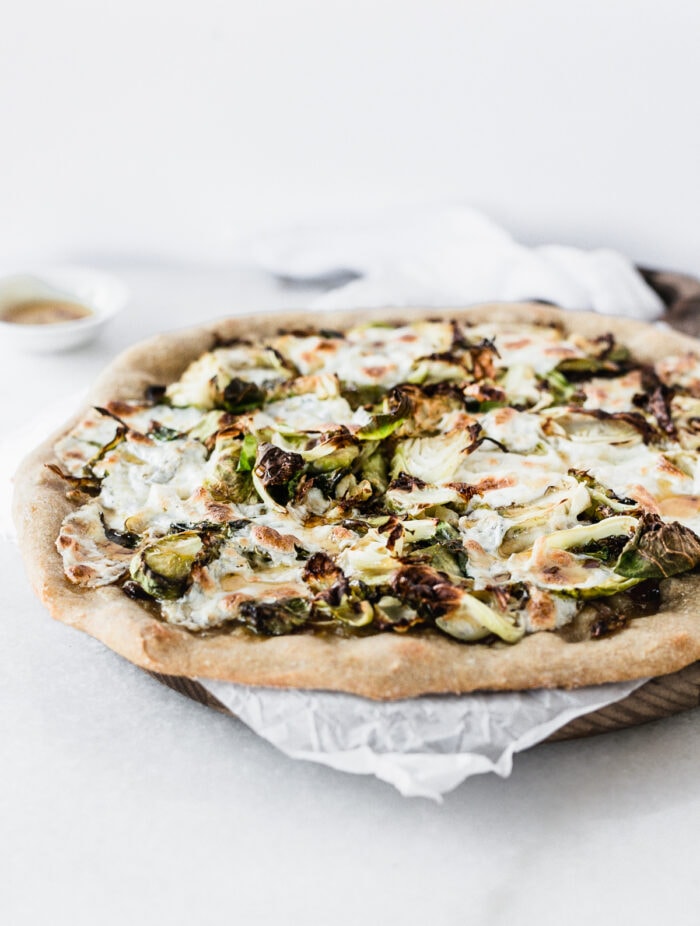 whole caramelized onion brussels sprout pizza on a wooden serving board lined with parchment.