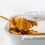 gold spoon lifting a piece of cinnamon ginger carrot souffle from a baking dish.