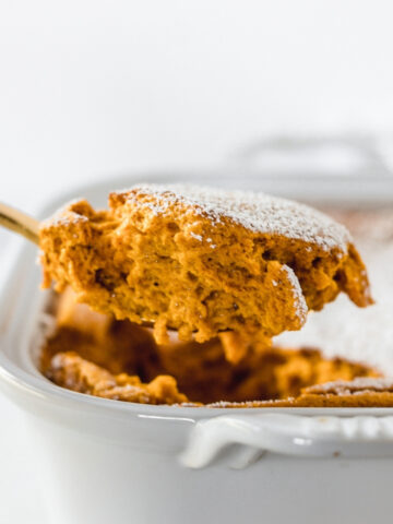 gold spoon lifting a piece of cinnamon ginger carrot souffle from a baking dish.