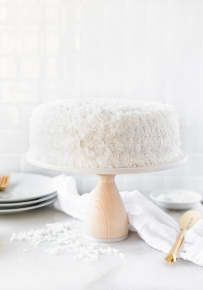 coconut cake on a white cake stand with a wood base.