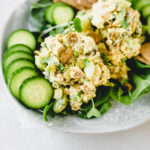 coconut curry chicken salad and sliced cucumbers on top of greens on a plate.