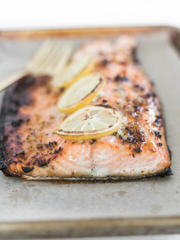 Closeup view of easy honey garlic salmon on parchment paper on a pan with lemon slices on top.