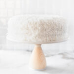 coconut cake on a white cake stand with a wood base.