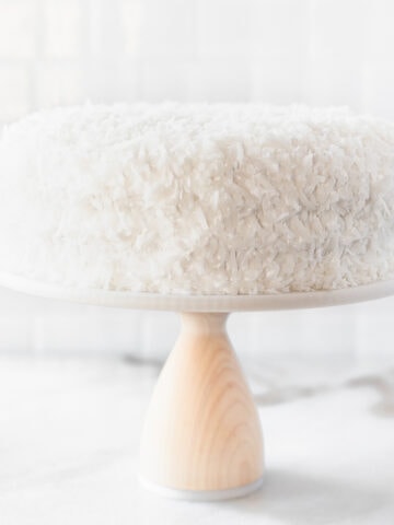 coconut cake on a white cake stand with a wood base.